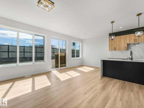 Open-concept living area featuring light wood-finish flooring, a modern kitchen island with pendant lighting, and a white tile backsplash - 272 Munn Way, Leduc, AB - Indoor Photo Showing Kitchen
