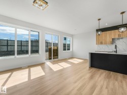 Open-concept living area featuring light wood-finish flooring, a modern kitchen island with pendant lighting, and a white tile backsplash - 