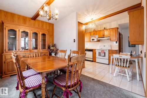 Dining area featuring wood-paneled accent walls, a classic chandelier, and an open concept layout to the kitchen - 8612 68A Street, Edmonton, AB - Indoor Photo Showing Dining Room