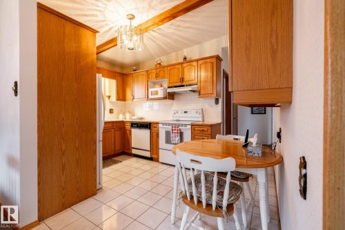 Eat-in kitchen featuring wood-finish cabinetry, white tile flooring, recessed lighting, and a crystal chandelier - 8612 68A Street, Edmonton, AB - Indoor Photo Showing Kitchen