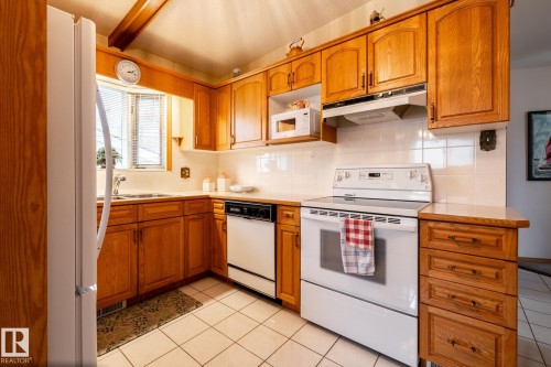 Kitchen featuring wood cabinetry, white appliances, tile flooring, tile backsplash, and a window above the sink - 8612 68A Street, Edmonton, AB - Indoor Photo Showing Kitchen With Double Sink