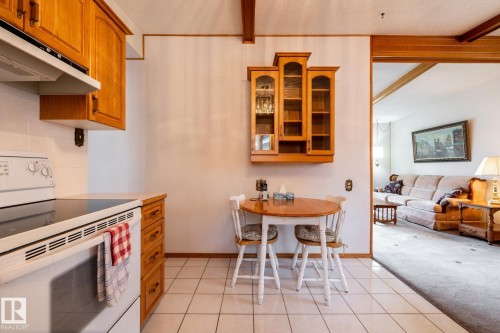 Kitchen area featuring wood cabinetry, white tile flooring, and a white electric range with overhead ventilation - 8612 68A Street, Edmonton, AB - Indoor Photo Showing Kitchen