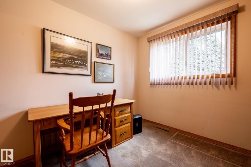 Carpeted room featuring a large window with vertical blinds, wood-frame window trim, and a light-toned wall finish - 8612 68A Street, Edmonton, AB - Indoor