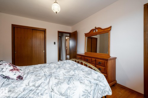 Bedroom featuring wood-finish flooring, white walls, and a built-in closet with sliding wood doors - 8612 68A Street, Edmonton, AB - Indoor Photo Showing Bedroom