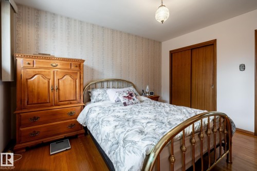 Interior space featuring wood-finish flooring, patterned wallpaper, a built-in closet with sliding wood doors, and a decorative ceiling light fixture - 8612 68A Street, Edmonton, AB - Indoor Photo Showing Bedroom