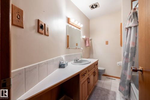 Bathroom featuring a built-in wood-finish vanity with a white countertop and integrated sink, accompanied by a rectangular mirror with strip lighting - 8612 68A Street, Edmonton, AB - Indoor Photo Showing Bathroom