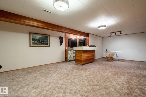 Spacious recreational area featuring a built-in bar with wood-finish paneling and a light-toned countertop - 8612 68A Street, Edmonton, AB - Indoor