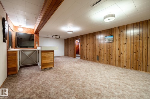 Recreation room featuring full-wall wood paneling, light-toned carpeting, and a built-in wet bar with wood cabinetry and a shelving unit - 8612 68A Street, Edmonton, AB - Indoor
