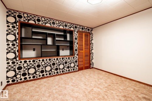 Room featuring a built-in shelving unit with varied compartments, a patterned accent wall, light-colored carpeting, white painted walls, and wooden bi-fold doors - 8612 68A Street, Edmonton, AB - Indoor Photo Showing Other Room