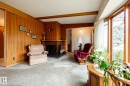 Living area featuring wood-paneled walls, a brick fireplace with a dark hearth, and a large bay window - 8612 68A Street, Edmonton, AB  - Indoor 