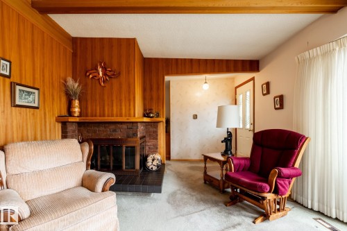 Living area featuring a brick fireplace with a black tile hearth and wood-paneled walls - 8612 68A Street, Edmonton, AB - Indoor Photo Showing Living Room With Fireplace