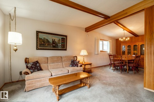 Carpeted living area featuring exposed ceiling beams and a hanging chain pendant light - 8612 68A Street, Edmonton, AB - Indoor Photo Showing Living Room