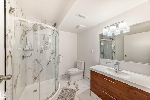 Bathroom featuring a curved glass shower enclosure with marbled wall tile, a modern wood-finish vanity with an integrated sink, a large mirror, and contemporary lighting fixtures - 2039 48 Street, Edmonton, AB - Indoor Photo Showing Bathroom