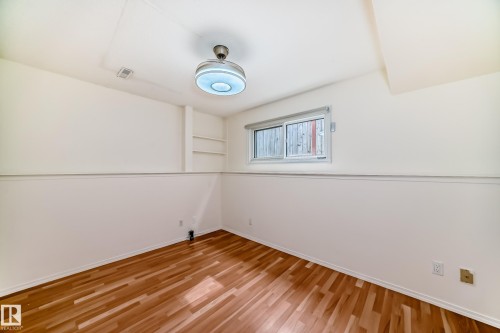 Room featuring wood-finish flooring, a two-tone wall treatment, built-in shelving, and a single window with a roller shade - 2039 48 Street, Edmonton, AB - Indoor Photo Showing Other Room