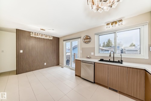 Contemporary kitchen and dining area featuring wood-finish cabinetry, a large window above the sink, stainless steel dishwasher, and a glass sliding door - 2039 48 Street, Edmonton, AB - Indoor Photo Showing Kitchen