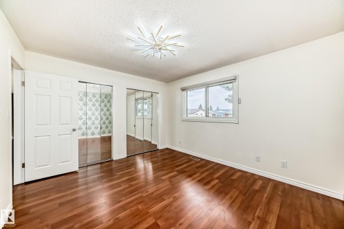 Room featuring wood-finish flooring, two sets of mirrored closet doors, a contemporary ceiling light fixture, and a window with a roller shade - 2039 48 Street, Edmonton, AB - Indoor Photo Showing Other Room