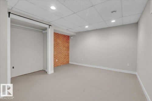 Unfurnished bedroom featuring a paneled ceiling, concrete flooring, a closet, recessed lighting, and brick wall - 3515 20 Avenue, Edmonton, AB - Indoor