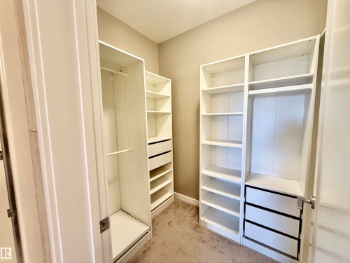 Walk-in closet featuring white built-in storage units, integrated shelving, hanging rods, and pull-out drawers - 437 5504 Schonsee Drive, Edmonton, AB - Indoor Photo Showing Other Room