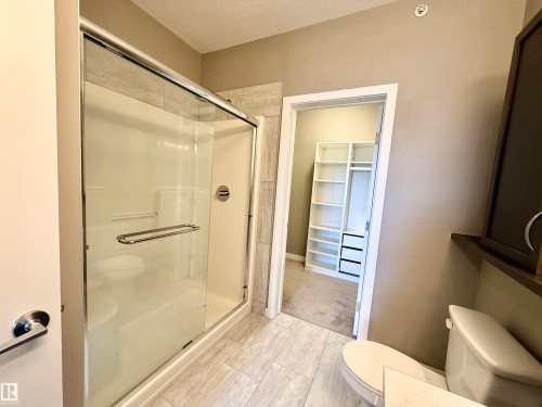 Glass-enclosed shower with chrome fixtures, light-toned wall tile, and a spacious walk-in closet with built-in shelving and drawers - 437 5504 Schonsee Drive, Edmonton, AB - Indoor Photo Showing Bathroom
