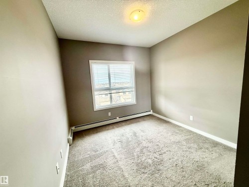 Carpeted room with a ceiling-mounted light fixture, neutral-toned walls, and a window featuring horizontal blinds - 437 5504 Schonsee Drive, Edmonton, AB - Indoor Photo Showing Other Room