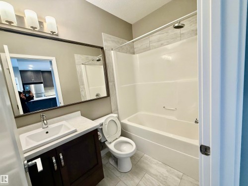Full bathroom featuring a dark wood-finish vanity with an integrated sink, a rectangular framed mirror, and a wall-mounted light fixture - 437 5504 Schonsee Drive, Edmonton, AB - Indoor Photo Showing Bathroom