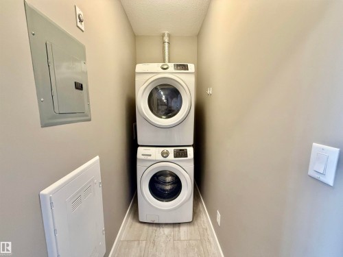 Dedicated laundry area featuring stacked front-load washer and dryer units, wood-finish tile flooring, and neutral wall paint - 437 5504 Schonsee Drive, Edmonton, AB - Indoor Photo Showing Laundry Room