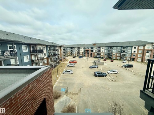 Residential building exterior featuring multi-toned siding, private balconies with black railings, and a large central parking area - 437 5504 Schonsee Drive, Edmonton, AB - Outdoor With Balcony