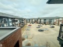Residential building exterior featuring multi-toned siding, private balconies with black railings, and a large central parking area - 437 5504 Schonsee Drive, Edmonton, AB  - Outdoor With Balcony 