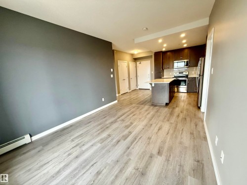 Open-concept living area featuring wood-finish flooring, a contemporary dark accent wall, and a kitchen with rich wood cabinetry - 437 5504 Schonsee Drive, Edmonton, AB - Indoor