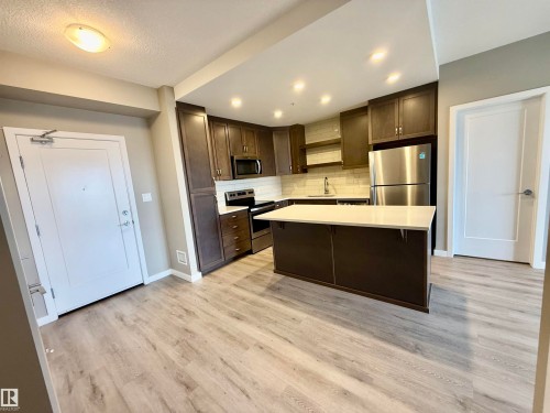 Contemporary kitchen featuring dark wood cabinetry, stainless steel appliances, a white subway tile backsplash, recessed lighting, and a kitchen island with a light-toned countertop - 437 5504 Schonsee Drive, Edmonton, AB - Indoor Photo Showing Kitchen With Upgraded Kitchen