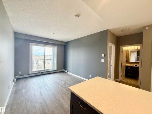 Spacious living area featuring wood-finish flooring, a sliding glass door leading to a balcony, and contemporary gray walls - 437 5504 Schonsee Drive, Edmonton, AB - Indoor Photo Showing Other Room
