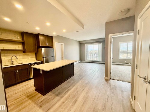 Open-concept living space featuring wood-finish flooring, a kitchen island with a light-toned countertop, dark wood cabinetry, and stainless steel appliances - 437 5504 Schonsee Drive, Edmonton, AB - Indoor Photo Showing Kitchen