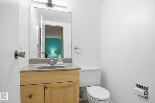 Bathroom featuring a light wood-finish vanity with a stone-finish countertop, undermount sink, and a large mirror with integrated lighting - 103 10732 86 Avenue, Edmonton, AB - Indoor Photo Showing Bathroom