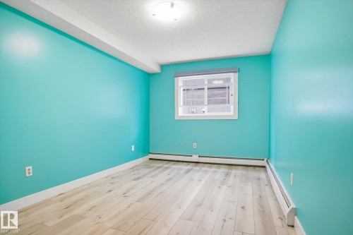Room featuring light wood-finish flooring, vibrant turquoise walls, and white baseboards - 103 10732 86 Avenue, Edmonton, AB - Indoor Photo Showing Other Room