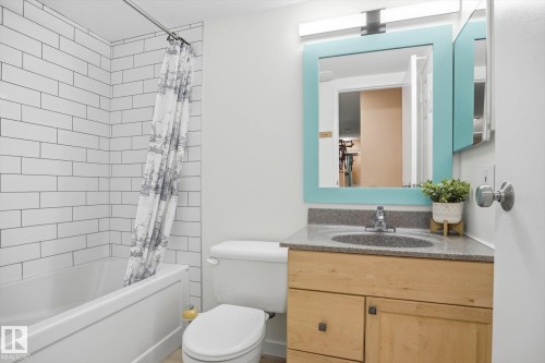 Bathroom featuring a porcelain tub, white subway tile surround, wood-finish vanity with a stone countertop, and a framed mirror with integrated lighting - 103 10732 86 Avenue, Edmonton, AB - Indoor Photo Showing Bathroom