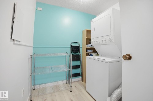 Dedicated laundry area featuring a stacked washer and dryer unit, wood-finish flooring, built-in shelving, and light blue wall accents - 103 10732 86 Avenue, Edmonton, AB - Indoor Photo Showing Laundry Room