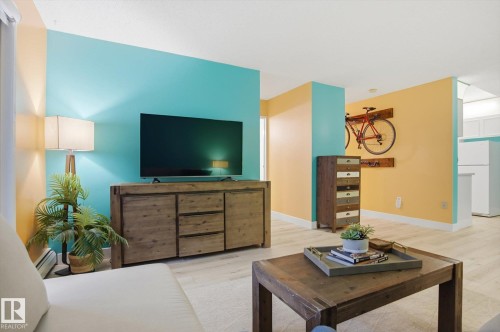 Open-concept living area with light wood-finish flooring, two-tone painted walls, and a large built-in entertainment console - 103 10732 86 Avenue, Edmonton, AB - Indoor Photo Showing Living Room