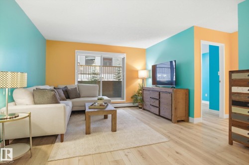 Living area with wood-finish flooring, a sliding glass door, and a light-colored area rug - 103 10732 86 Avenue, Edmonton, AB - Indoor Photo Showing Living Room