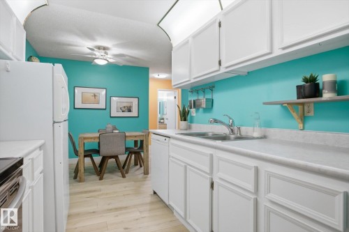 Kitchen featuring white cabinetry, light-toned countertops, a double basin stainless steel sink, and wood-finish flooring - 103 10732 86 Avenue, Edmonton, AB - Indoor Photo Showing Kitchen With Double Sink