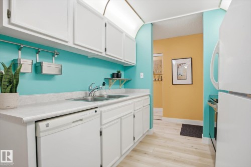 Kitchen featuring white cabinetry, light-toned wood-finish flooring, and white countertops - 103 10732 86 Avenue, Edmonton, AB - Indoor Photo Showing Kitchen With Double Sink