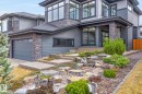 Modern exterior featuring multiple large windows, a stone and siding facade, an integrated garage, and a tiered rock garden with plantings - 1313 Hainstock Way, Edmonton, AB  - Outdoor 
