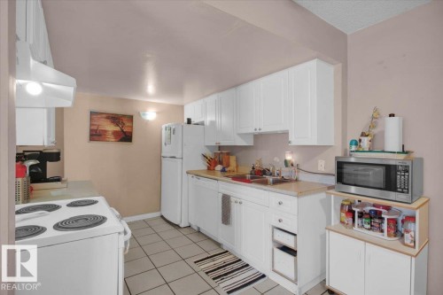 The kitchen features white cabinetry, a refrigerator, a dishwasher, a range, and tile flooring - 412 2908 116A Avenue, Edmonton, AB - Indoor Photo Showing Kitchen With Double Sink