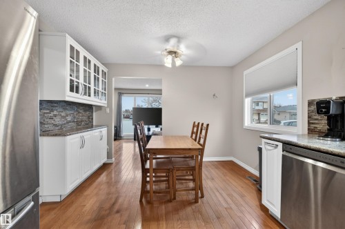 Kitchen and dining area featuring wood-finish flooring, white cabinetry with glass-front uppers, a mosaic tile backsplash, and light-toned countertops - 17120 103 Street, Edmonton, AB - Indoor