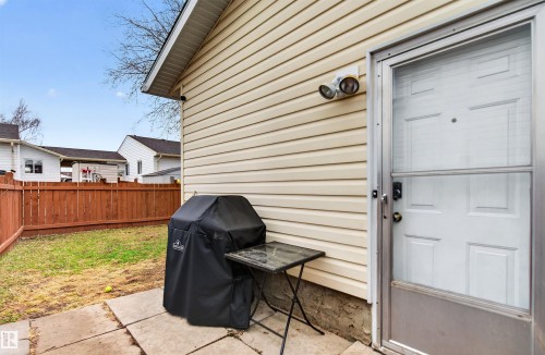 Rear exterior featuring cream-colored siding, a white paneled door with a storm door, and an exterior light fixture - 17120 103 Street, Edmonton, AB - Outdoor With Exterior