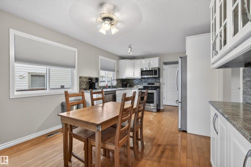Open-concept kitchen and dining area featuring warm wood-finish flooring, white cabinetry, stainless steel appliances, and a mosaic tile backsplash - 17120 103 Street, Edmonton, AB - Indoor
