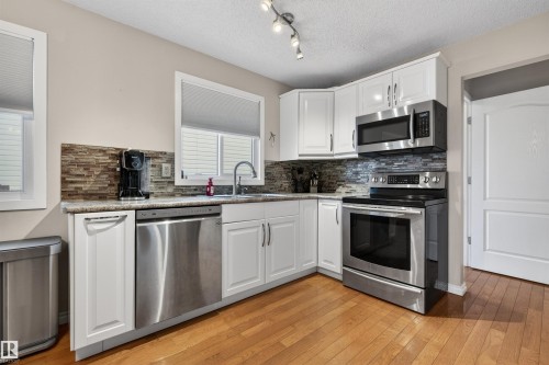 Kitchen featuring white cabinetry, stainless steel appliances, a tile backsplash, light-toned countertops, and wood-finish flooring - 17120 103 Street, Edmonton, AB - Indoor Photo Showing Kitchen With Stainless Steel Kitchen