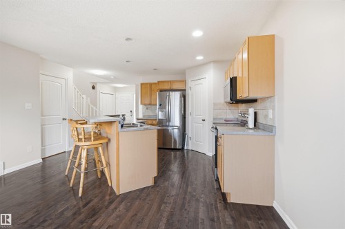 Open-concept kitchen featuring wood-finish flooring, light wood cabinetry, stainless steel appliances, and a breakfast bar with stone-look countertops - 1124 37A Avenue, Edmonton, AB - Indoor Photo Showing Kitchen With Double Sink