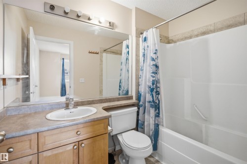 Full bathroom featuring a single vanity with wood-finish cabinetry, an integrated sink, and a large wall-mounted mirror - 1124 37A Avenue, Edmonton, AB - Indoor Photo Showing Bathroom