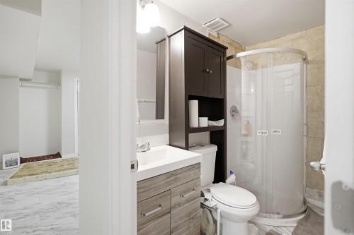Bathroom featuring a wood-finish vanity with an integrated sink, a dark wood storage cabinet, a toilet, and a stand-up shower with a curved glass enclosure - 1124 37A Avenue, Edmonton, AB - Indoor Photo Showing Bathroom