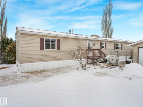 Rear exterior featuring tan horizontal siding, brown window shutters, and a rear entrance with a wood deck and stairs - 151 3400 48 Street, Stony Plain, AB - Outdoor